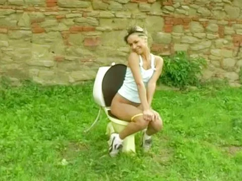 Teen Sandy is outdoors near the wall where she masturbates using a dildo